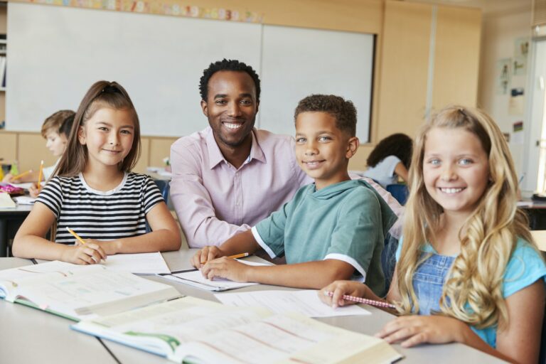 male-school-teacher-and-kids-in-class-smiling-to-camera.jpg